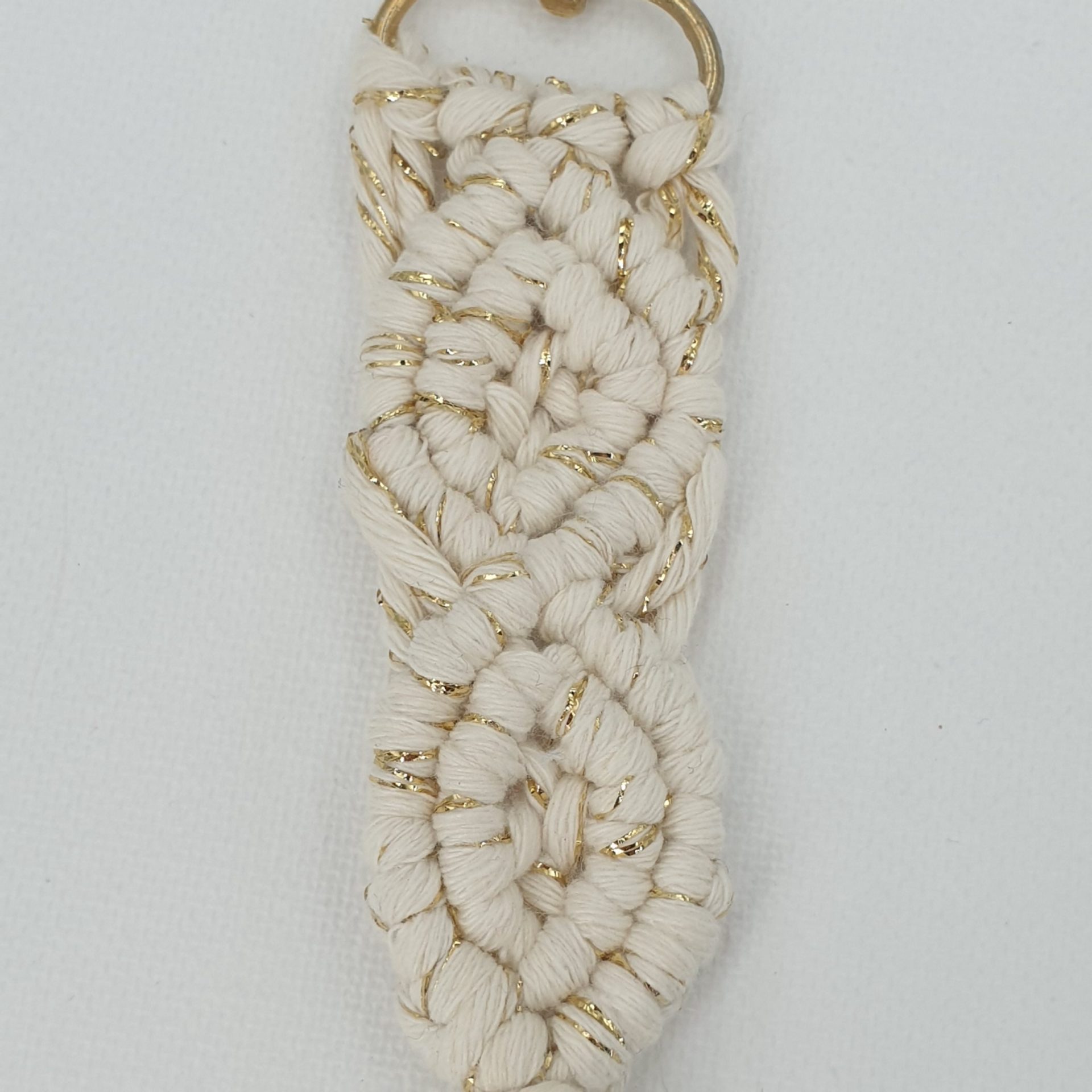 Gros plan sur le nouage du porte clé en macramé blanc et doré